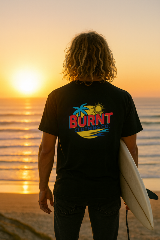Person wearing a black t-shirt with 'BURNIT' logo at sunset on the beach