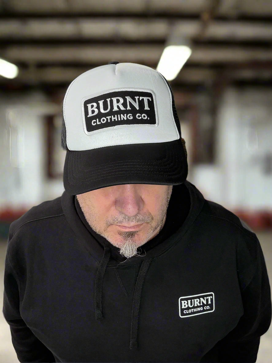 Person wearing a black hoodie and white cap with 'Burnt Clothing Co.' logo in a workshop setting.