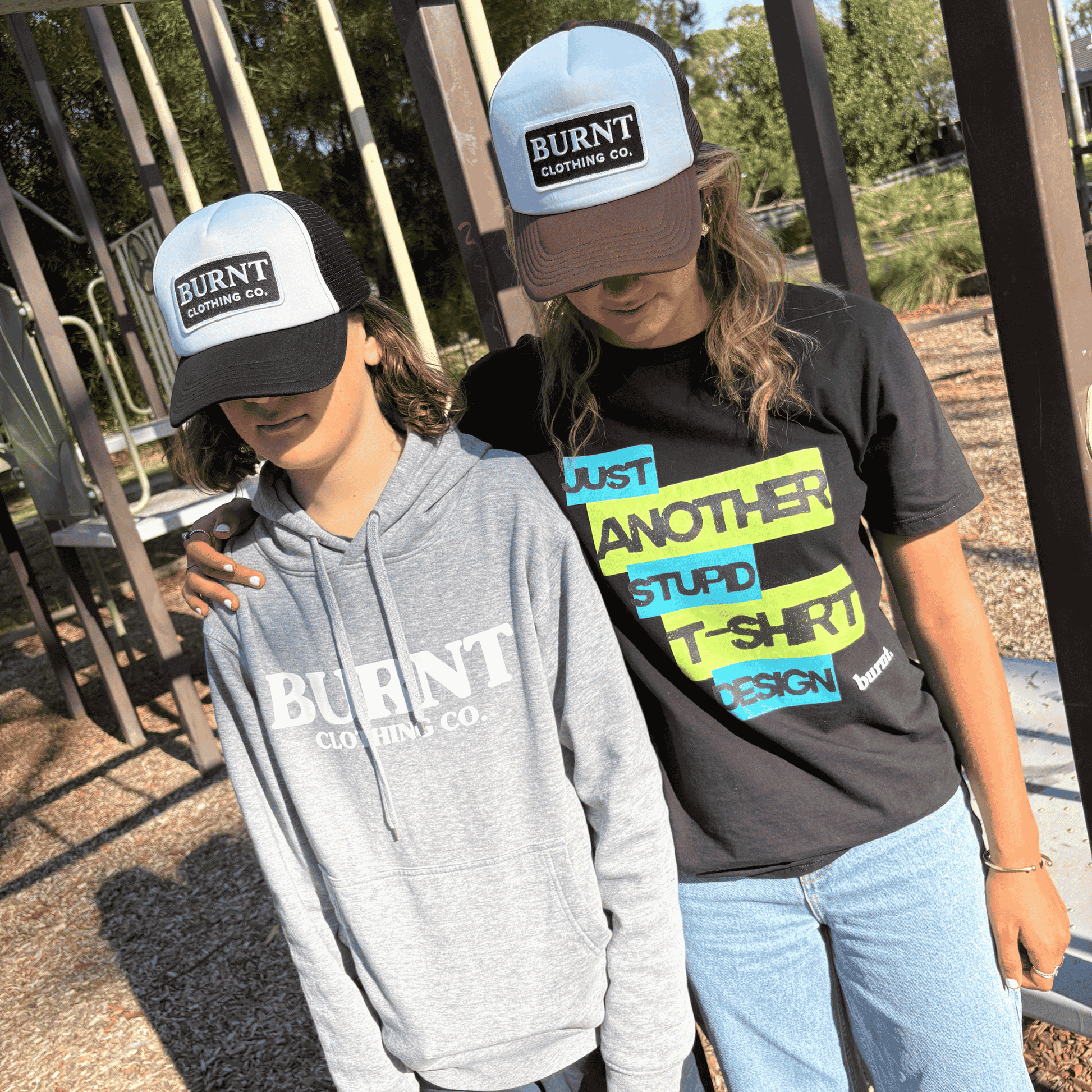 Two people wearing 'Burnt Clothing Co' branded hats and clothing outdoors.