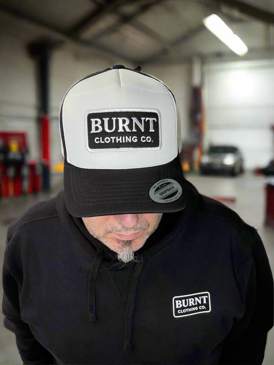 Person wearing a black 'Burnt Clothing Co.' cap and jacket in a workshop setting.