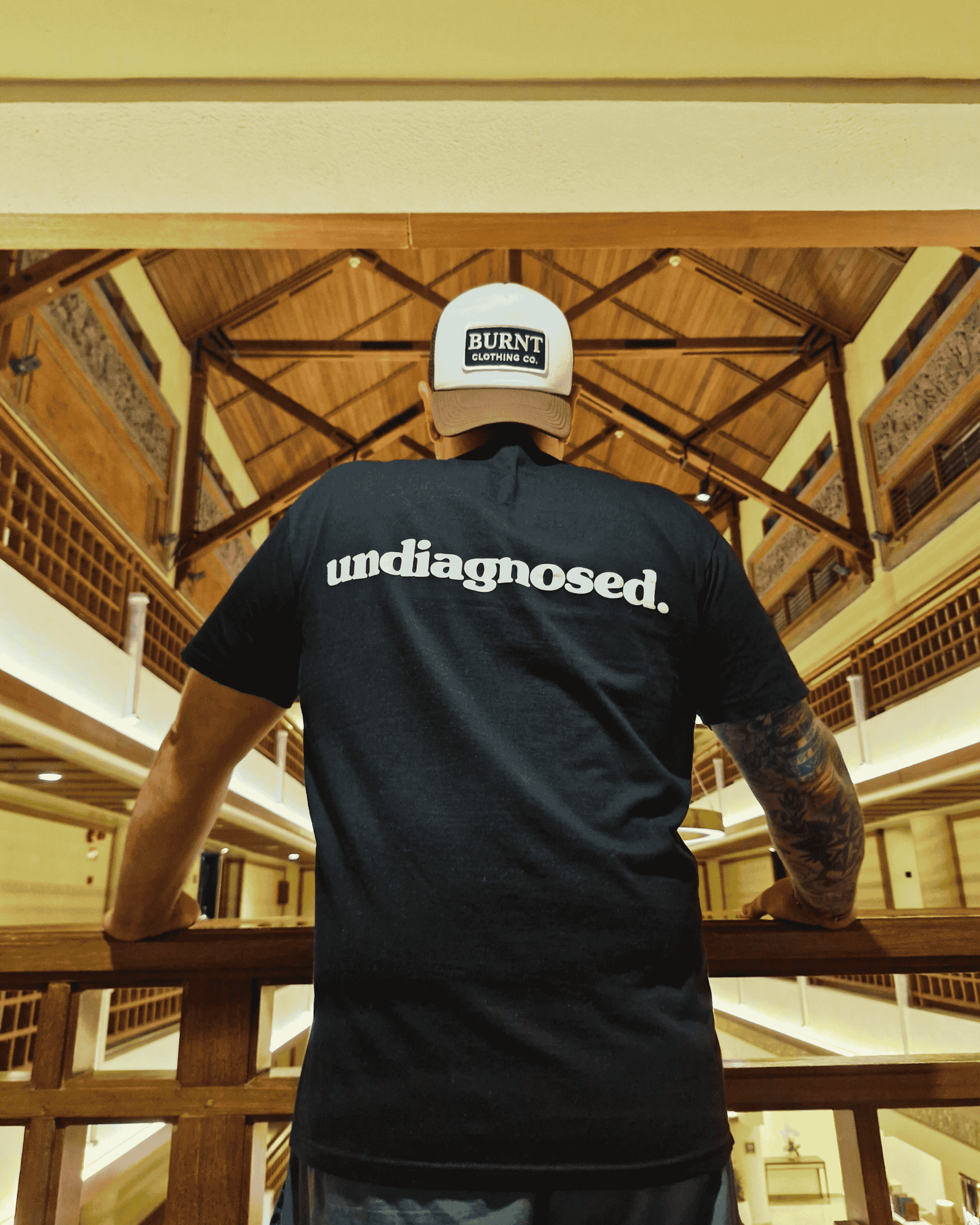 Person wearing a black t-shirt with 'undiagnosed.' text and a cap inside a building with wooden architecture.
