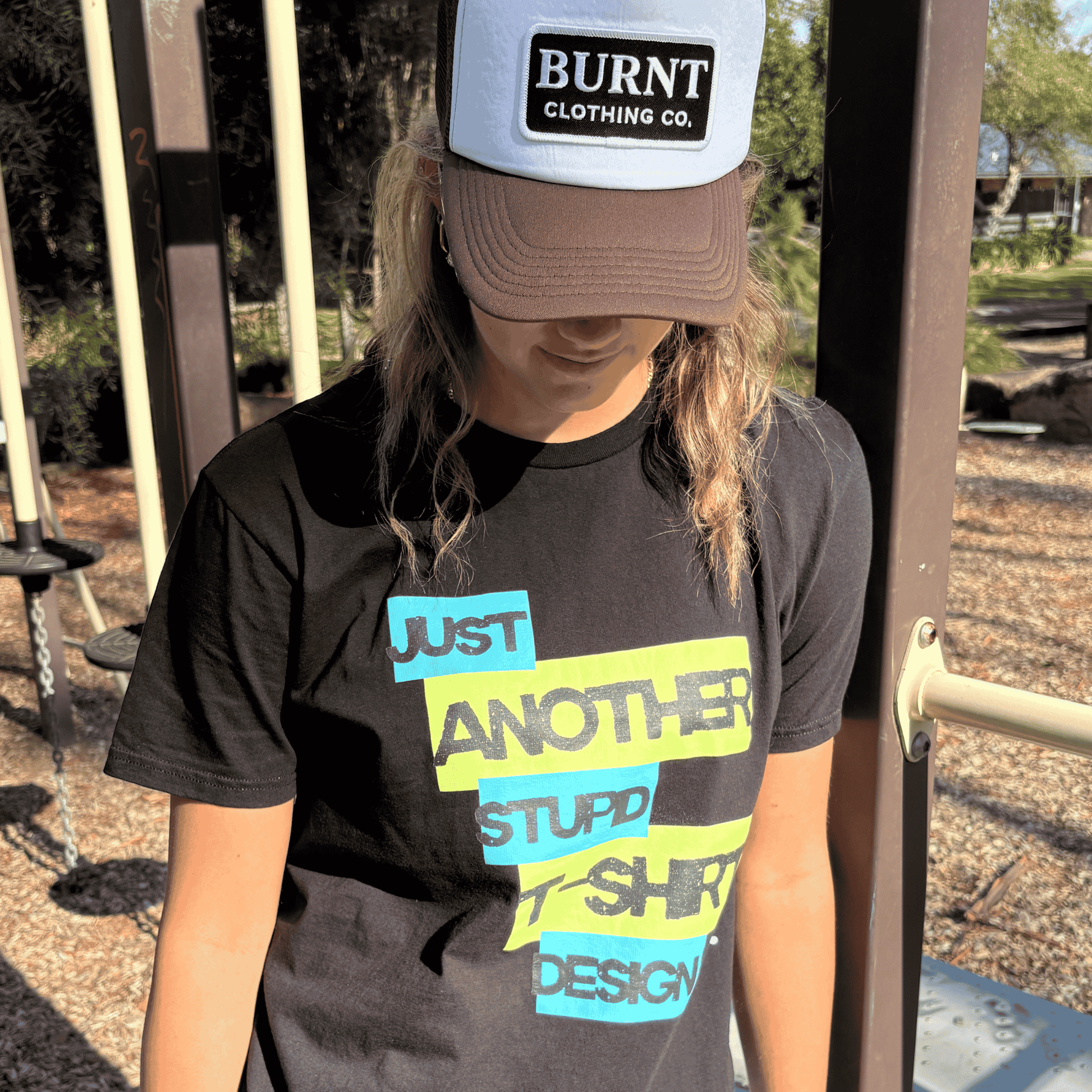 Person wearing Burnt Just Another Stupid T-Shirt Design graphic tee in black with Burnt Clothing Co. Trucker Cap