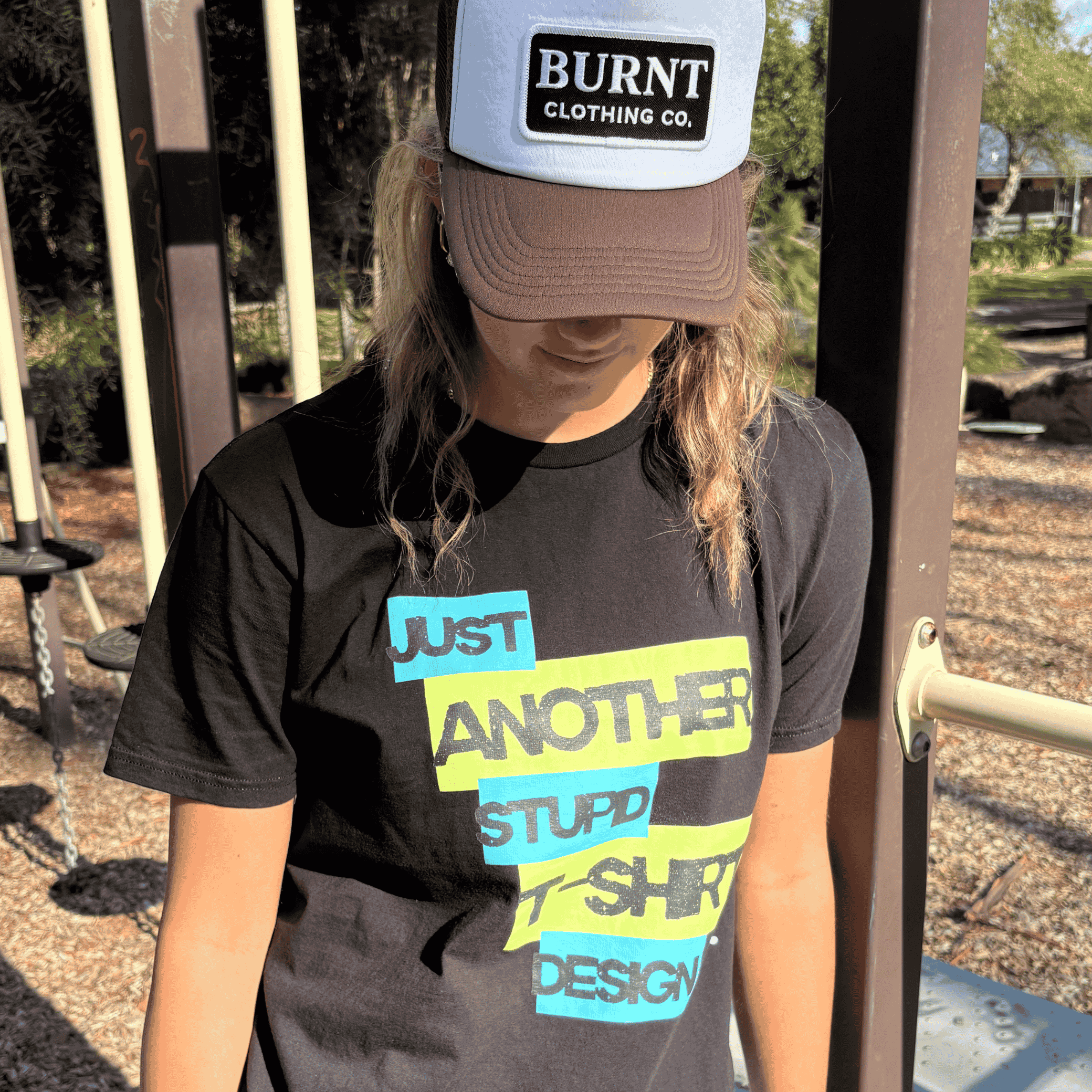 Person wearing Burnt Just Another Stupid T-Shirt Design graphic tee in black with Burnt Clothing Co. Trucker Cap