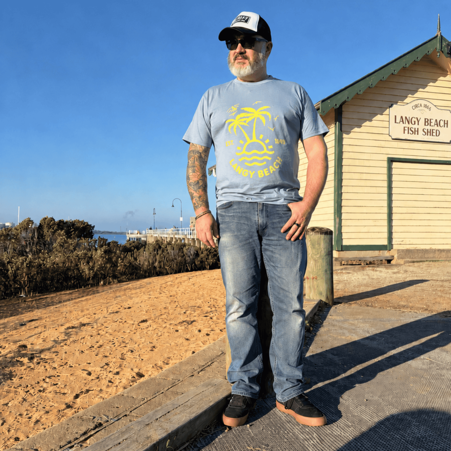 Man standing in front of the Langy Beach Fish Shed with a blue Langy beach t-shirt on. 