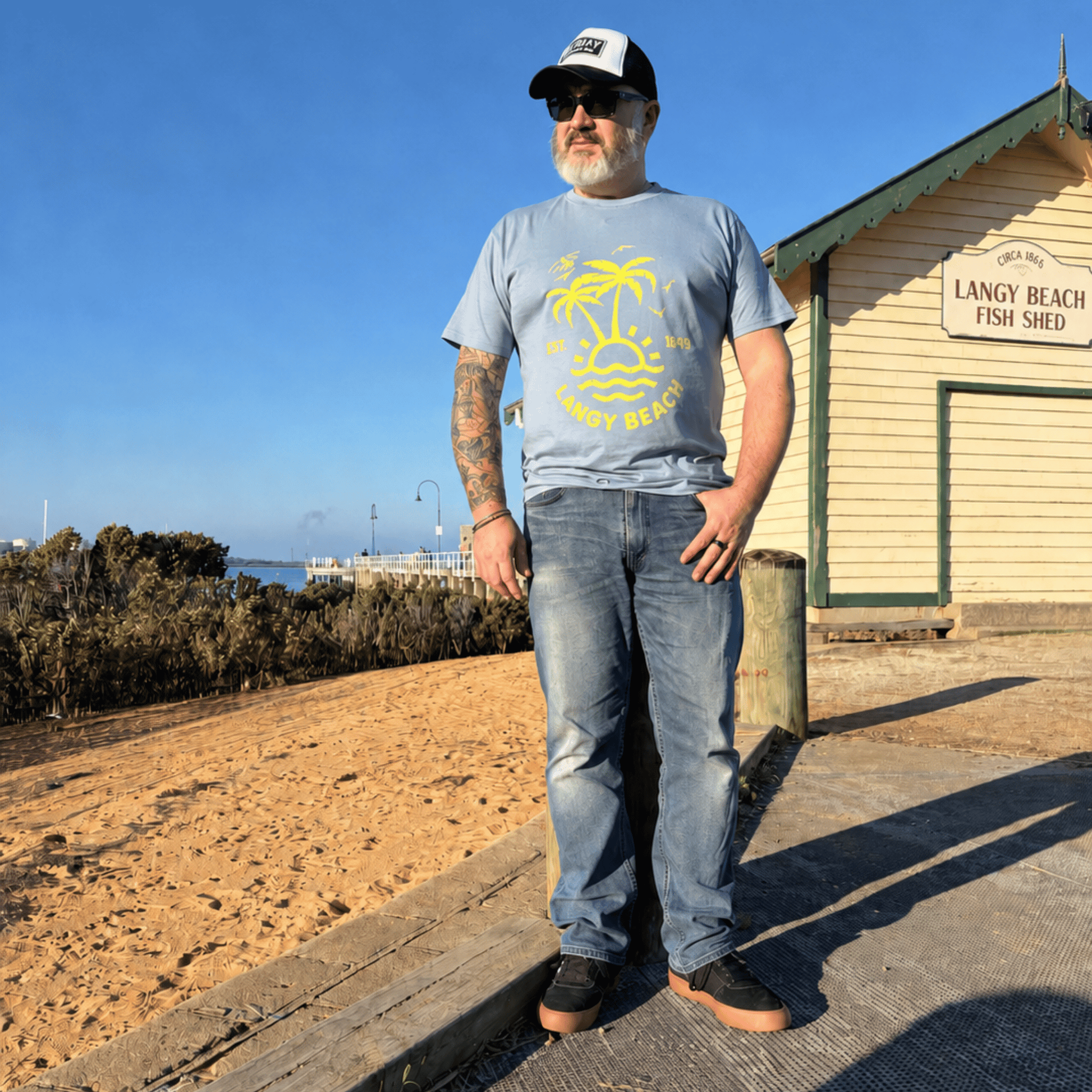 Man standing in front of the Langy Beach Fish Shed with a blue Langy beach t-shirt on. 