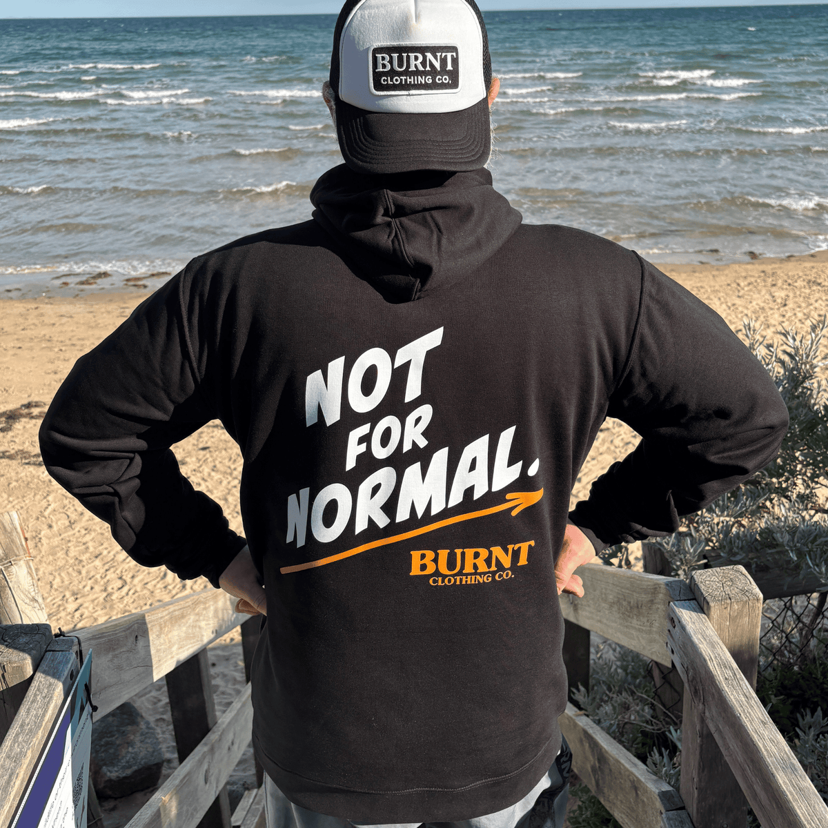 White and burnt-orange NOT FOR NORMAL graphic on the back of the black Statement hoodie.