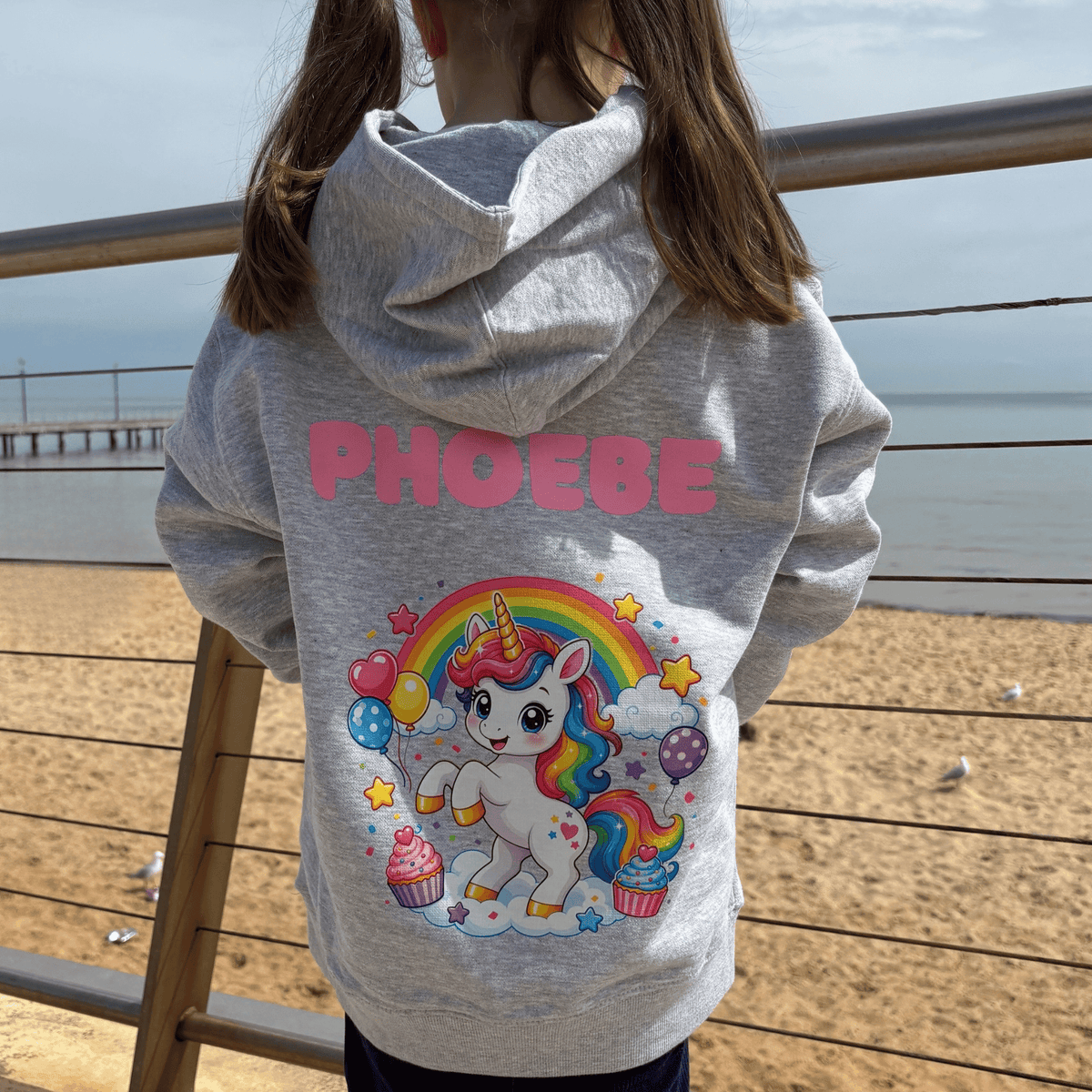 Child wearing grey Cupcake Unicorn personalised kids hoodie with pink name on back