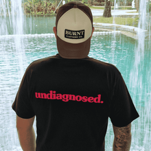 Model wearing black undiagnosed. t-shirt with pink statement print at a waterfall.