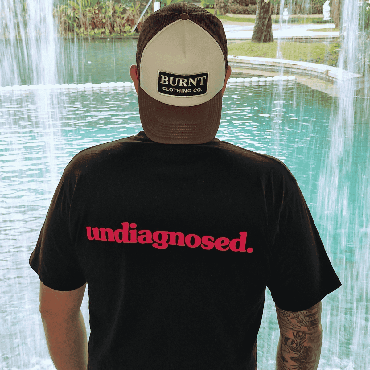 Model wearing black undiagnosed. t-shirt with pink statement print at a waterfall.