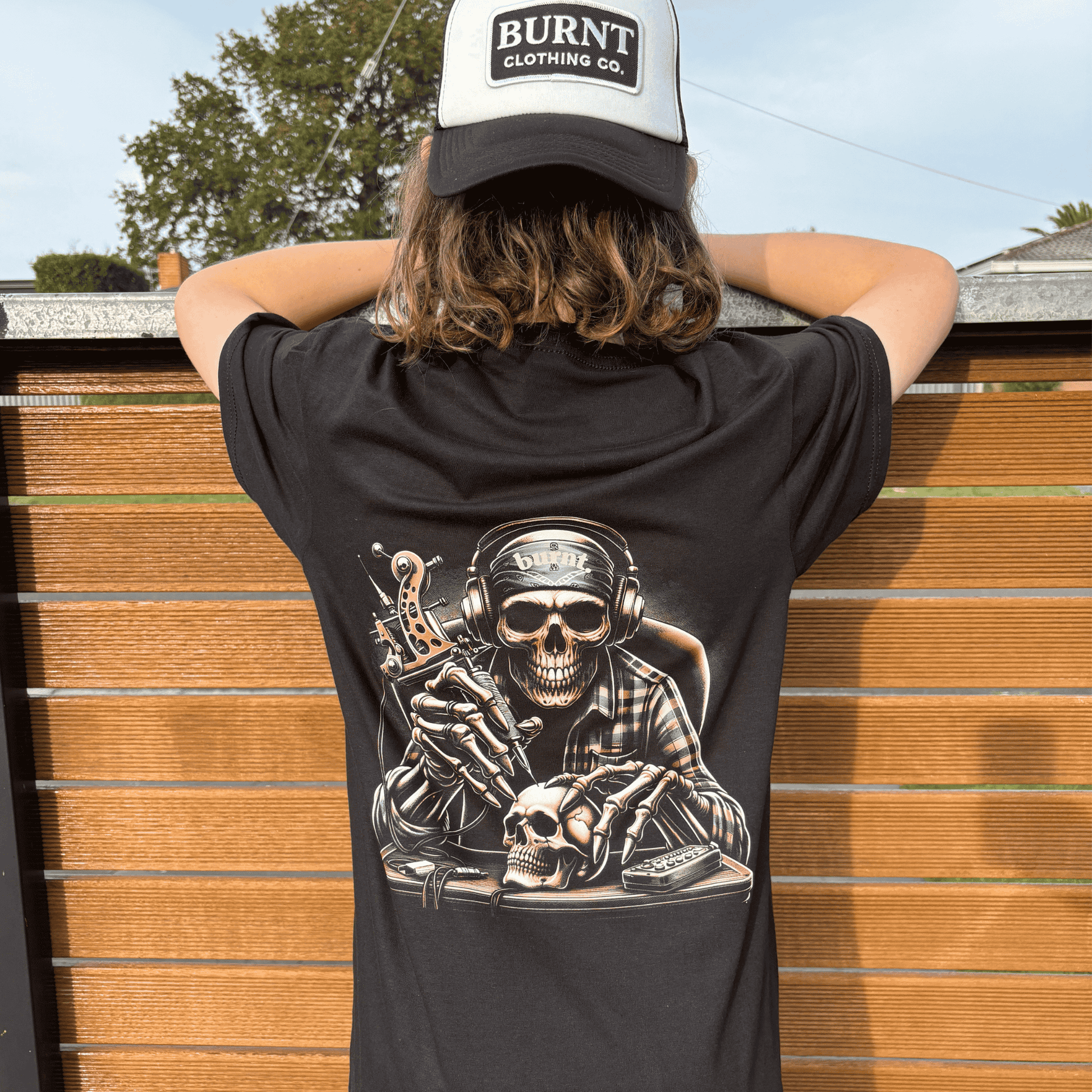 Burnt Clothing Co “Last Session” tee with skull tattoo artist graphic, worn by model with trucker cap