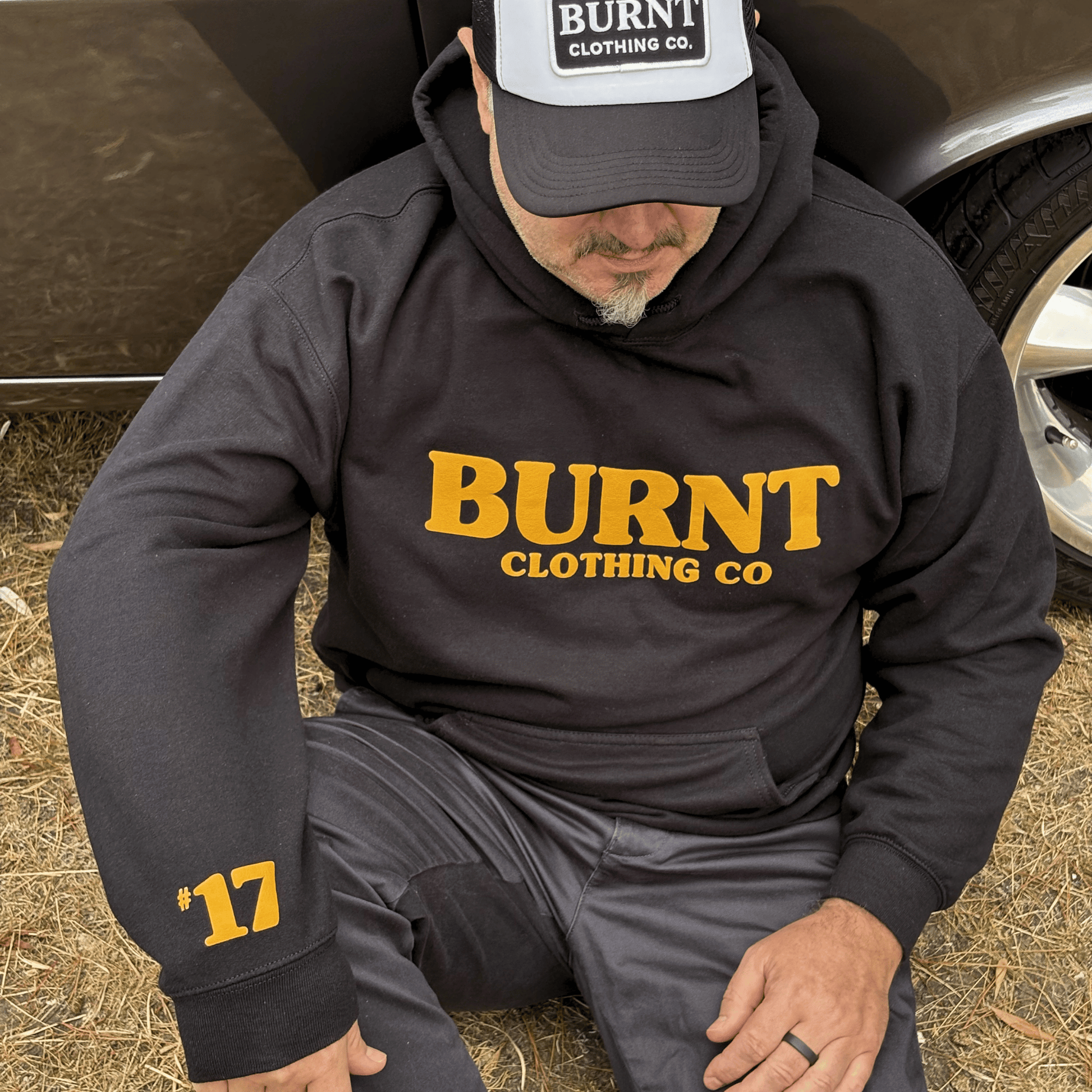 Person wearing a black hoodie with 'BURNT CLOTHING CO' text, sitting on the ground.