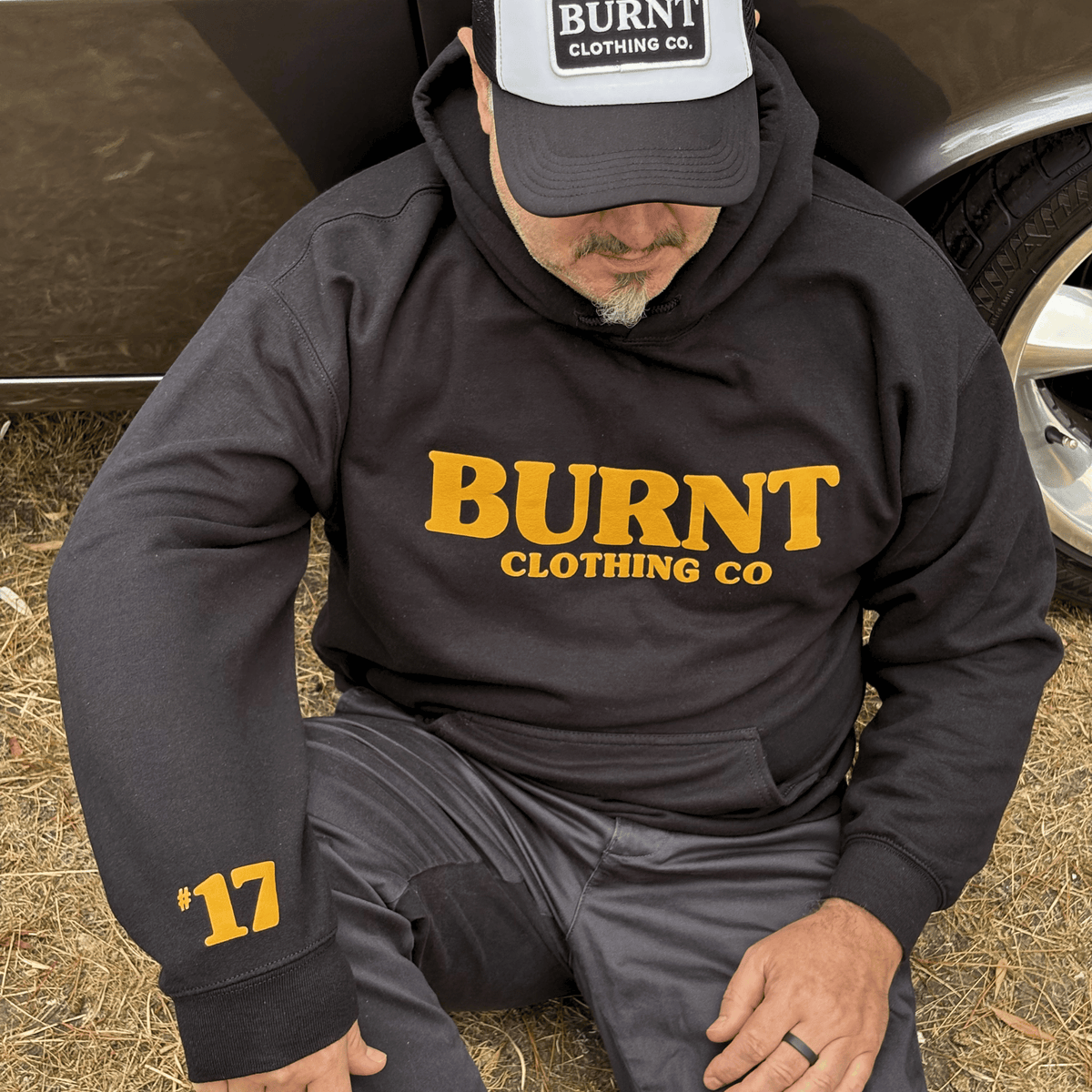 Person wearing a black hoodie with 'BURNT CLOTHING CO' text, sitting on the ground.