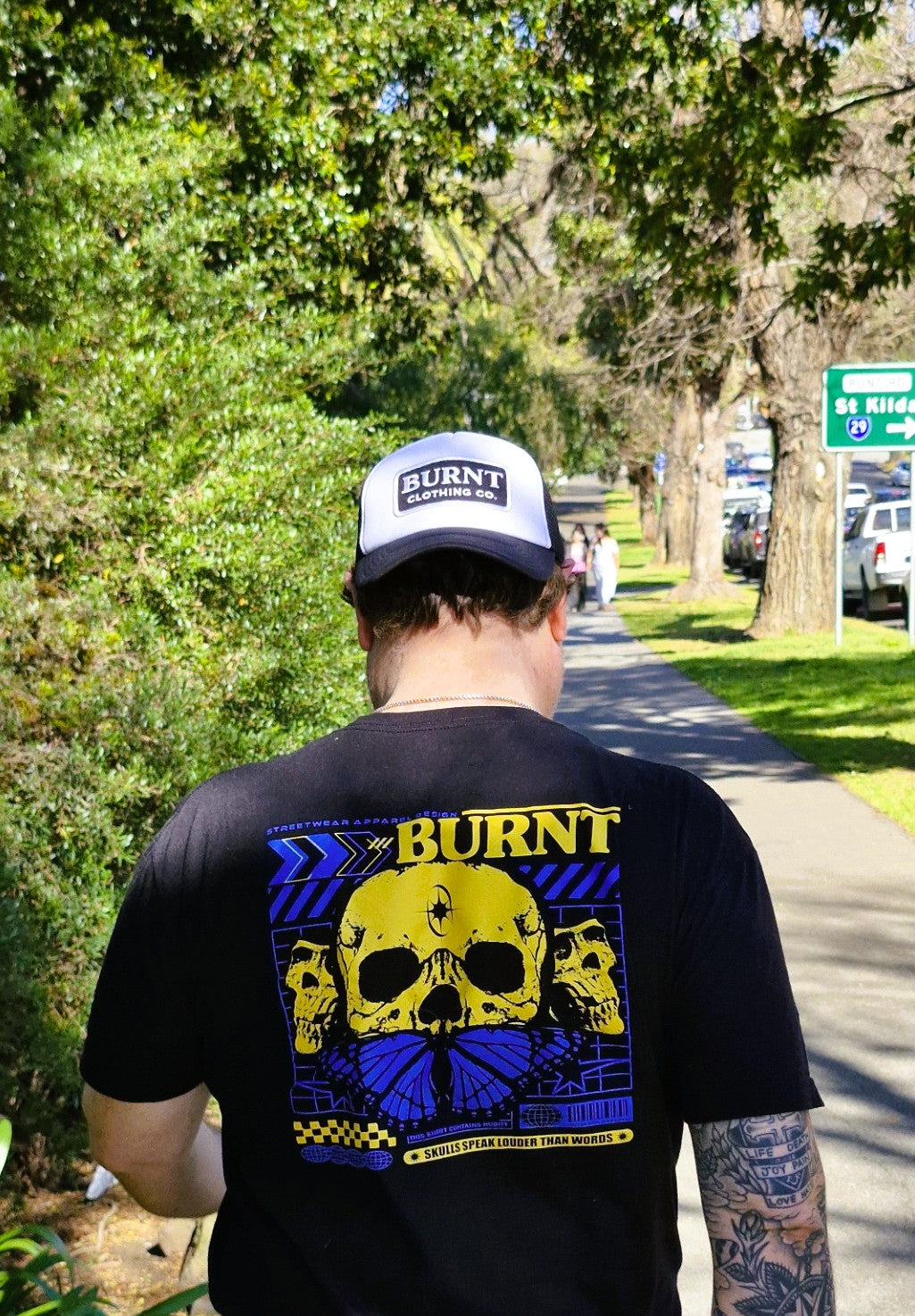 Person wearing a black 'Burnt' t-shirt with a skull design outdoors.
