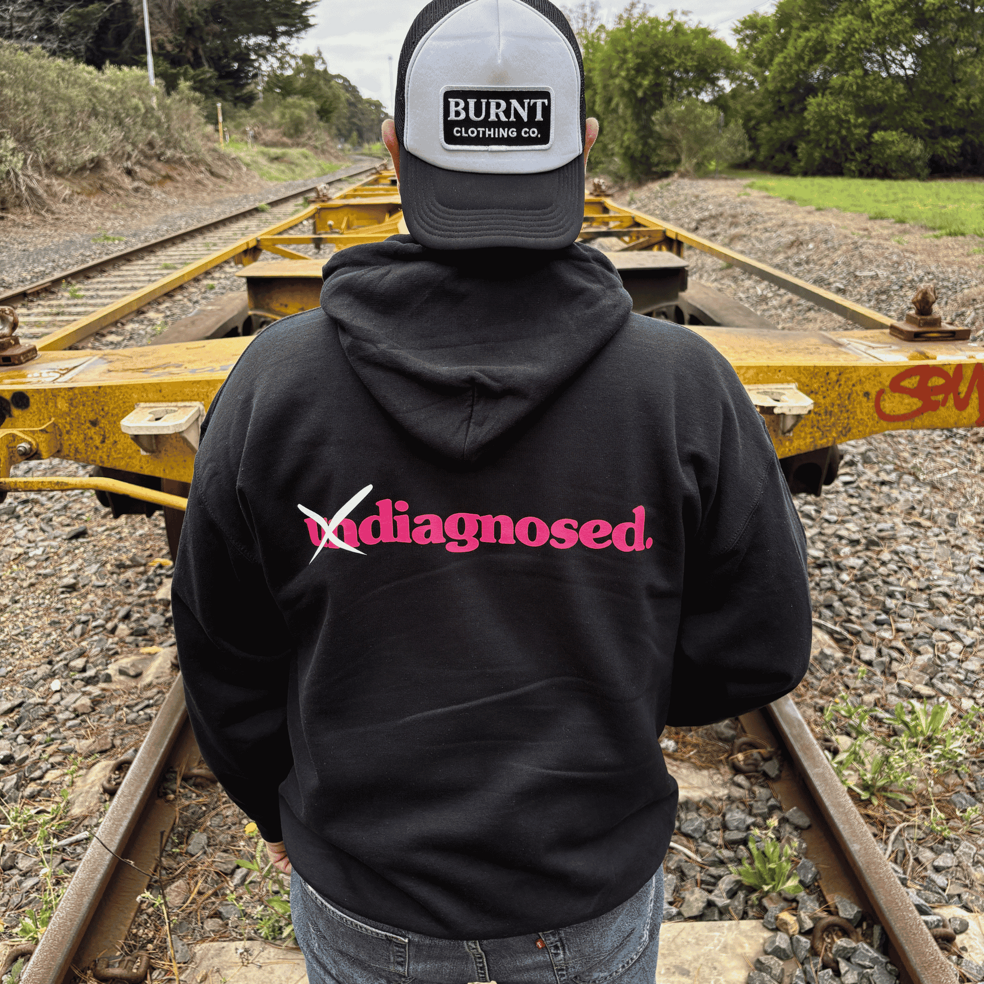 Back view of diagnosed. black hoodie with pink print by Burnt Clothing Co