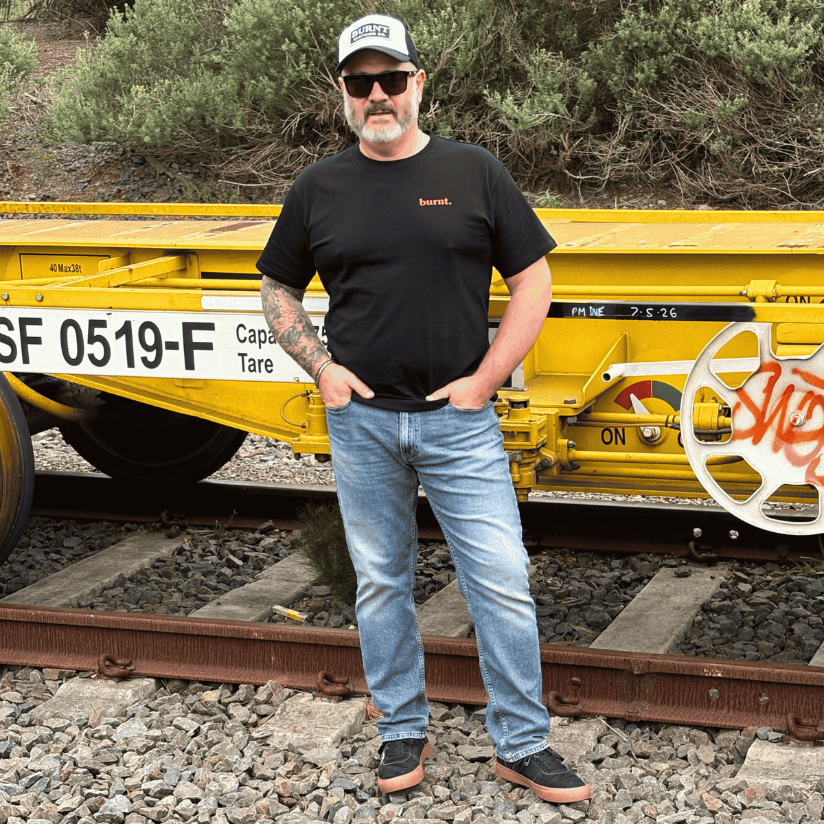 Man wearing the diagnosed. black graphic T-shirt beside a yellow railway car