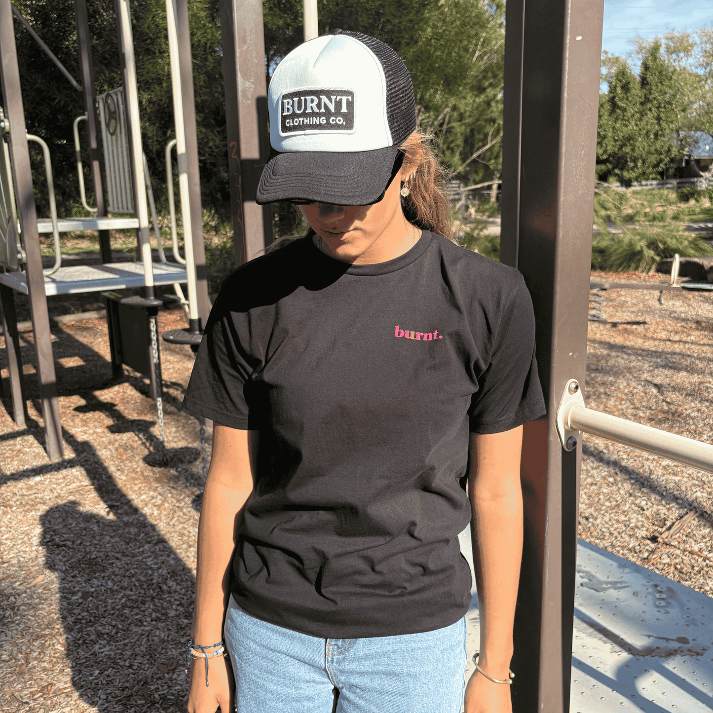 Person wearing black diagnosed. limited edition tee with small pink Burnt chest logo and Burnt Clothing Co. trucker cap outdoors.