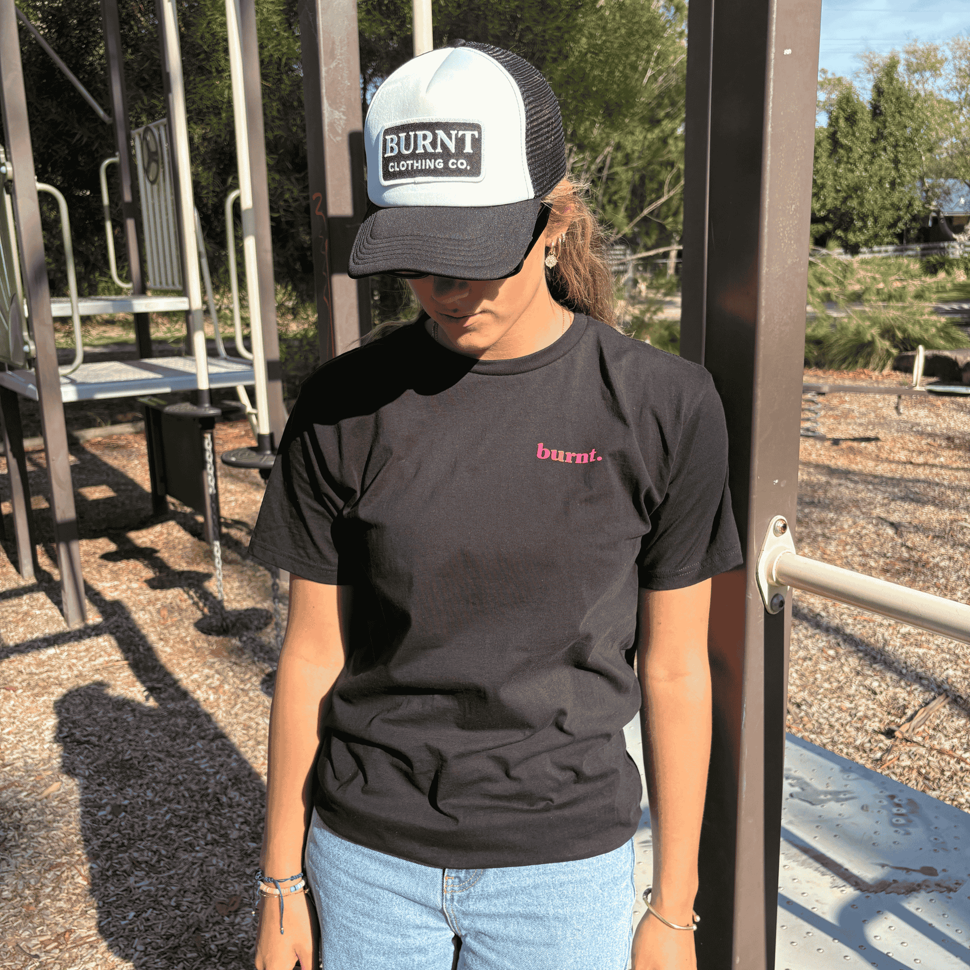 Person wearing black diagnosed. limited edition tee with small pink Burnt chest logo and Burnt Clothing Co. trucker cap outdoors.