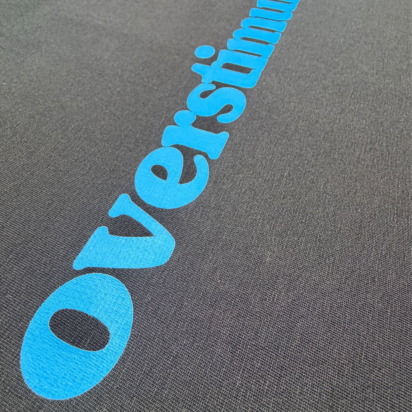 Close-up of the burnt electric blue overstimulated. print on a black cotton T-shirt.