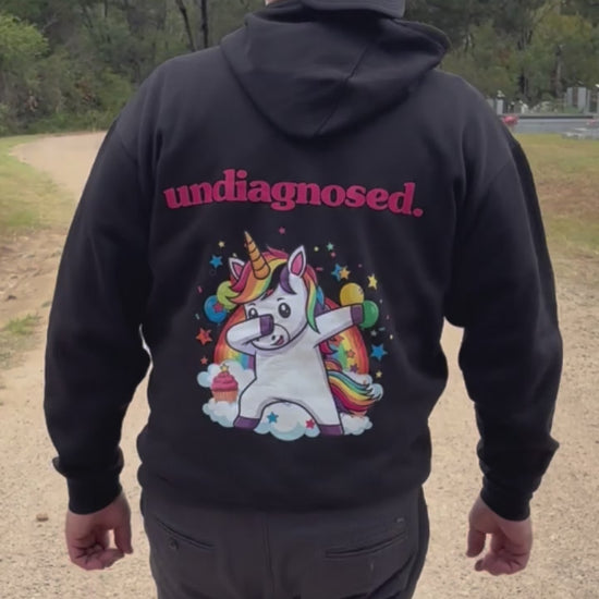 “Person walking away outdoors wearing a black undiagnosed. hoodie with pink lettering and a colourful unicorn graphic on the back.”