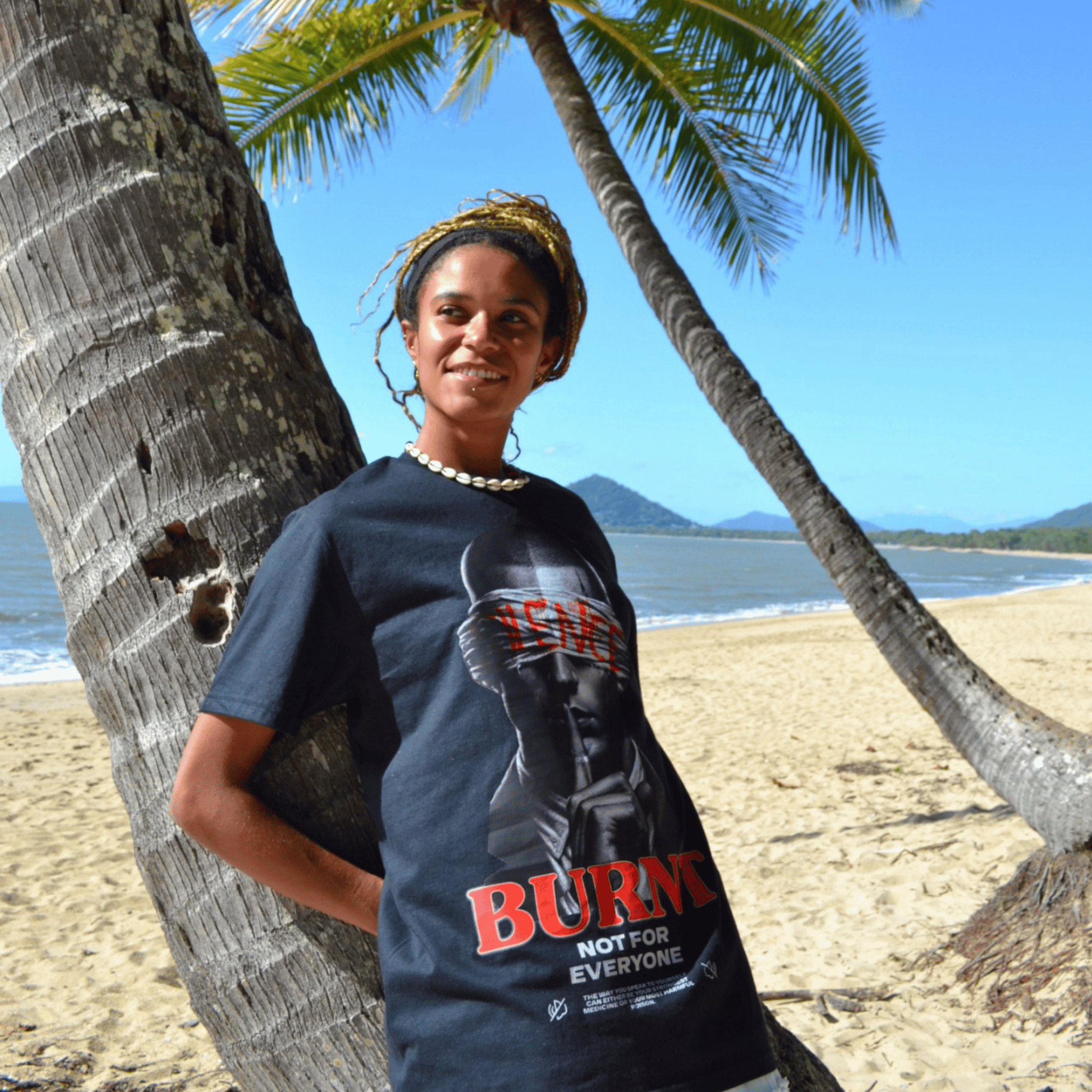 Model wearing The Quiet War black graphic tee near palm trees