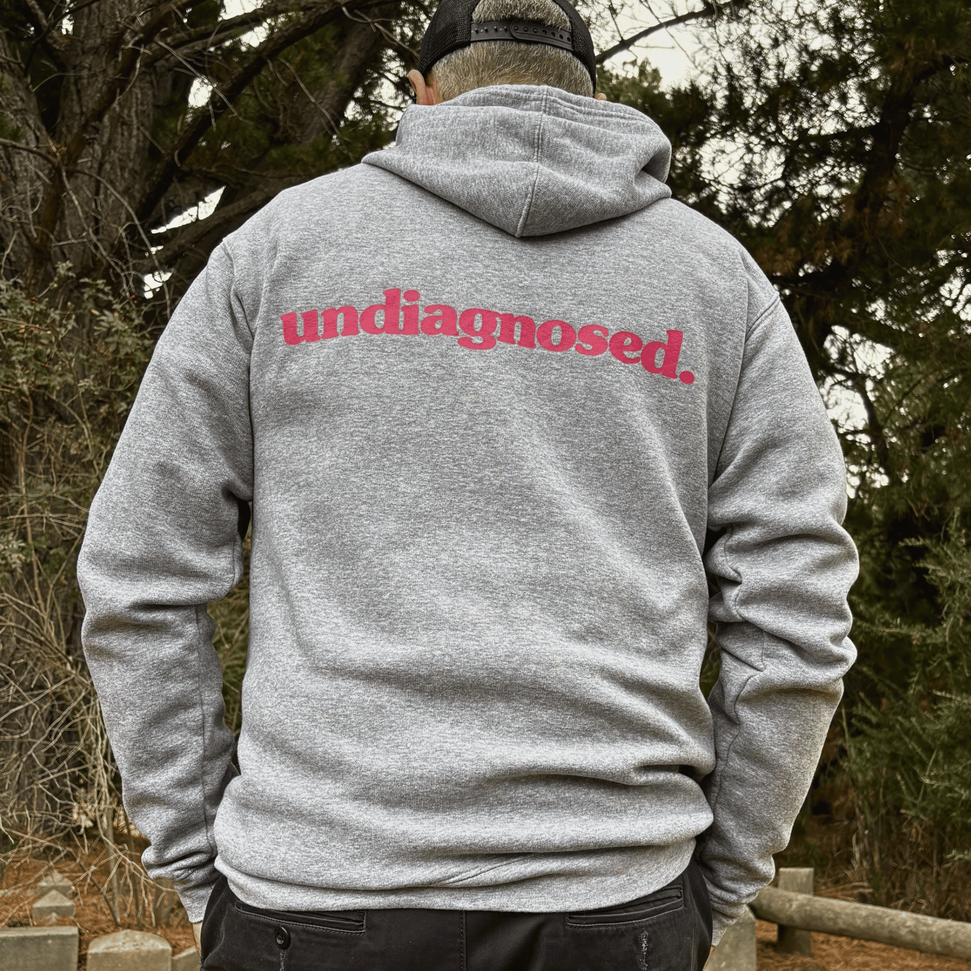 Model wearing the Burnt Clothing Co. undiagnosed. grey hoodie with pink back print outdoors.